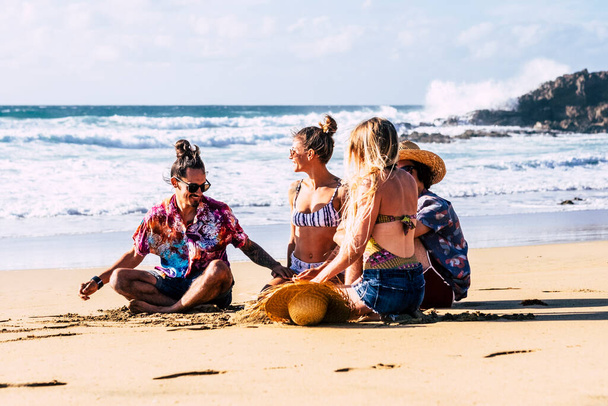 Група друзів туристів насолоджується літнім грайливим відпочинком на відкритому повітрі і відпусткою на пляжі, розмовляючи з дівчатами і багато сміючись разом у дружбі
.  - Фото, зображення