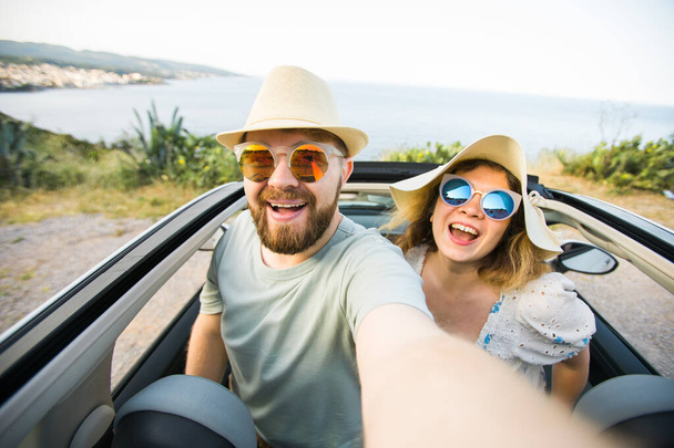 Mutlu ve güzel bir çift tatilde üstü açık bir arabayla selfie çektiriyorlar. Kiralık arabalar ve tatil konsepti - Fotoğraf, Görsel