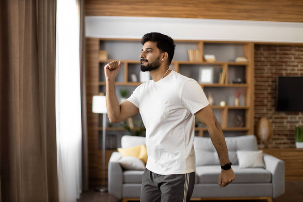 Handsome arabian man in short clothes making active fitness exercises at living room. Young bearded guy training muscles for fit body shape. Healthy lifestyles concept. - Fotoğraf, Görsel