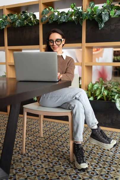 Woman Wearing Glasses using Laptop. Charming businesswoman in eyeglasses and casual clothes working with laptop computer watching screen. Elegant business female full length vertical shoot - Foto, Imagen