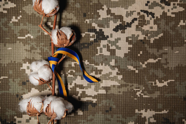 Ein Baumwollzweig mit einem Band aus blau-gelb, der Farbe der Flagge der Ukraine auf dem Hintergrund eines militärischen Pixels - Foto, Bild