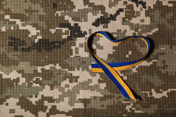 Синьо-жовта стрічка у формі серця на тлі військового камуфляжу. Поняття патріотизму, свободи і демократії
 - Фото, зображення
