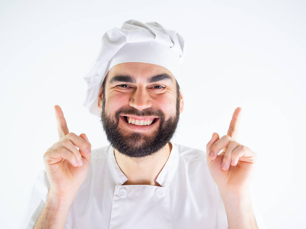 Genç aşçı, gülümseyip kameraya bakarken iki eliyle işaret ediyor. Beyaz bir arkaplanda izole edilmiş - Fotoğraf, Görsel