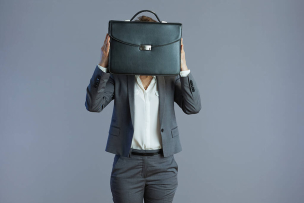 modern woman worker in grey suit with briefcase against gray background. - 写真・画像