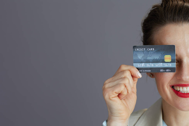 Closeup on happy woman worker in a light business suit with credit card isolated on grey. - Фото, изображение
