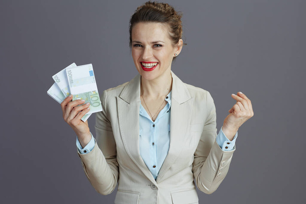 happy elegant small business owner woman in a light business suit with euros money packs isolated on gray background. - Fotoğraf, Görsel