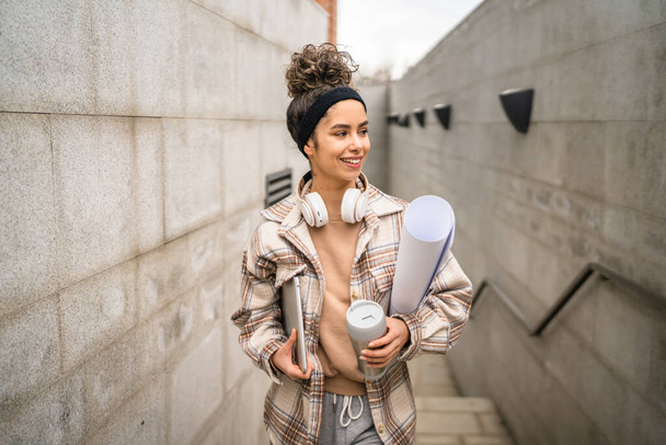 One woman young adult female student go to class outdoor hold laptop computer cup of coffee and work material real person coy space happy smile confident with headphones in day - Foto, Imagen