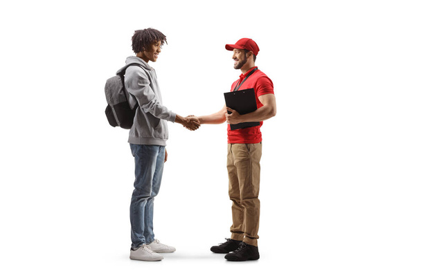 Full length profile shot of an african american young man  shaking hands with a delivery guy isolated on white background - Foto, Imagen