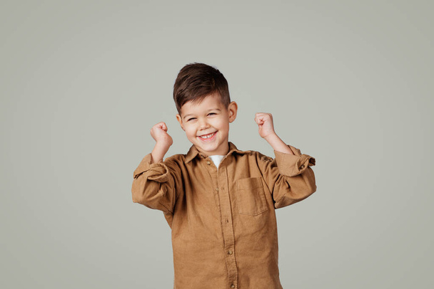 Onnellinen pieni eurooppalainen poika iloitsee voitosta, tekee menestyksen ele eristetty harmaa studio tausta. Oppilaiden tunteet, erinomainen opiskelu ja koulutus, mainonta ja tarjous - Valokuva, kuva