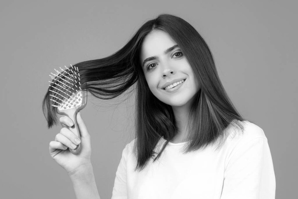 Beautiful woman combs her healthy hair. Combing healthy long straight female hair, close up - Фото, зображення