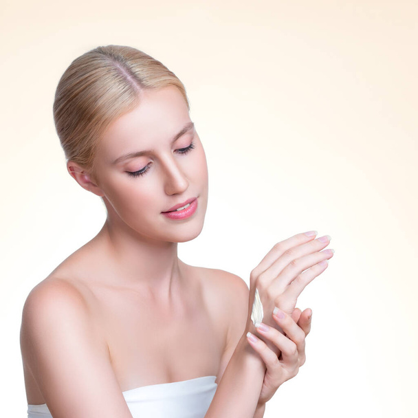 Personable woman applying moisturizer cream on her hand for perfect skincare treatment concept in isolated background. Beauty care cream applying on body by female model with soft natural makeup. - Photo, Image