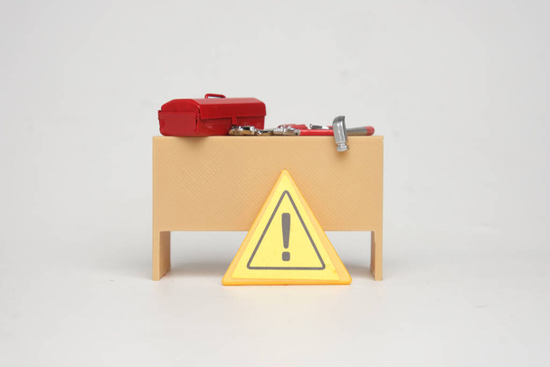 Una foto di scrivania in miniatura, cassetta degli attrezzi e strumenti con cartello di pericolo. Concetto di pericolo di lavoro. - Foto, immagini