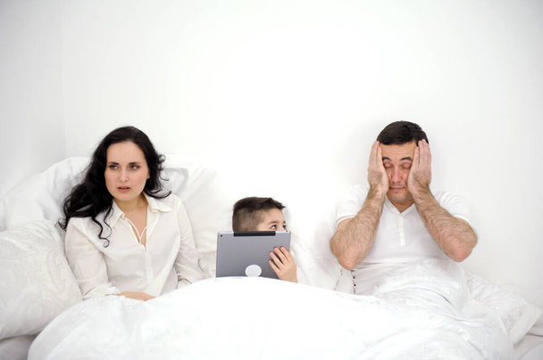 Eltern schwören Sohn sitzt am Computer keine Aufmerksamkeit für die Kinderprobleme im Familienstreit Frustriertes junges Paar mit ernsthaften Beziehungsproblemen auf dem Bett. - Foto, Bild
