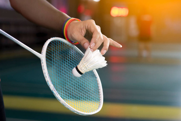 Badminton player wears rainbow wristbands and holding racket and white shuttlecock in front of the net before serving it to player in another side of the court, concept for LGBT people activities. - Photo, Image