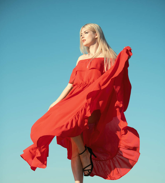 Woman in red dress movement on sky. Female model in a fashion dress outdoor - 写真・画像