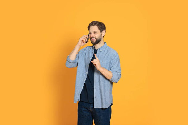 Ο άνθρωπος μιλάει στο smartphone με φόντο πορτοκαλί - Φωτογραφία, εικόνα