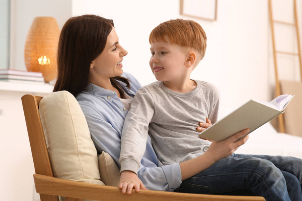 Mother reading book with her child on armchair at home - Photo, Image
