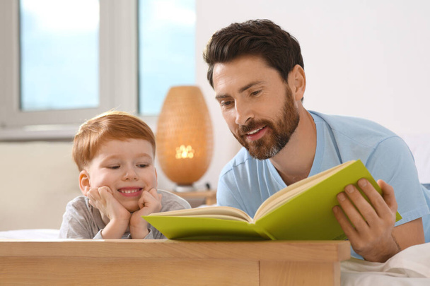 Father reading book with his child on bed at home - Photo, Image