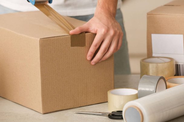 Man packing box with adhesive tape indoors, closeup - Foto, afbeelding
