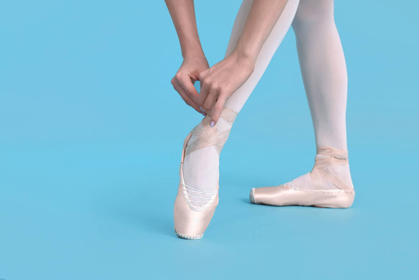 Young ballerina tying pointe shoes on light blue background, closeup - Foto, afbeelding