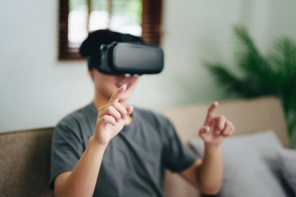 portrait of a young Asian man using virtual reality simulator headset at home. - Photo, Image