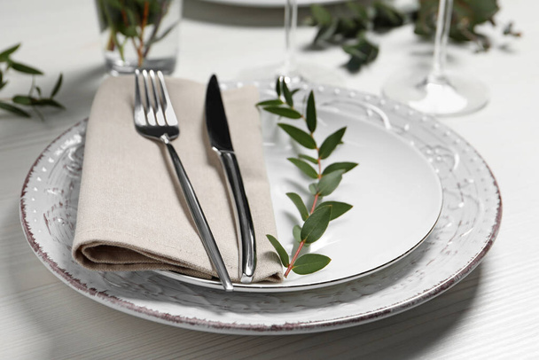 Stylish setting with cutlery and eucalyptus leaves on white wooden table, closeup - Фото, изображение
