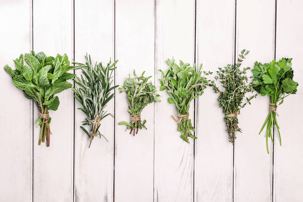 Bunches of fresh green herbs on white wooden table, top view - 写真・画像