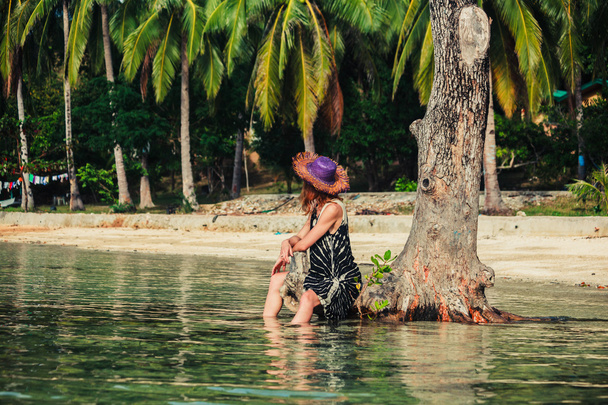 Femme assise contre un arbre sur une plage tropicale
 - Photo, image