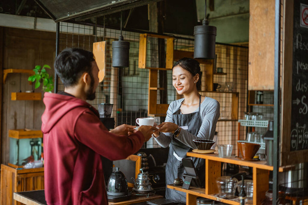 the male customer receiving the cup of coffee from the female barista that standing inside the bar desk - 写真・画像