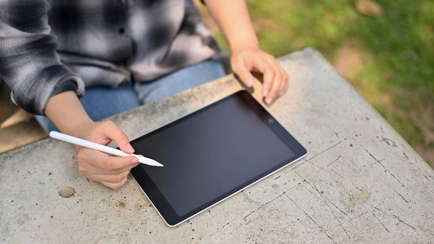 an Asian woman in flannel shirt using her digital tablet at the green park. people and technology concept. close-up image - Photo, Image