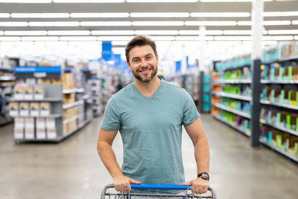 Portrait of hispanic man with shopping trolley purchasing in grocery store. Sales and shopping. Man buying products at supermarket. Supermarket and grocery shop. Discount, sale concept - Fotó, kép