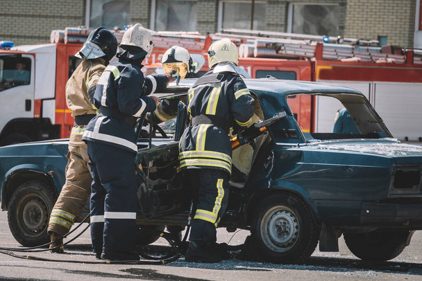 Palomies, jolla on suojahaalarit ja työkäsineet, kun rikot auton tuulilasia. ensiapu tieliikenneonnettomuuden jälkeen. - Valokuva, kuva