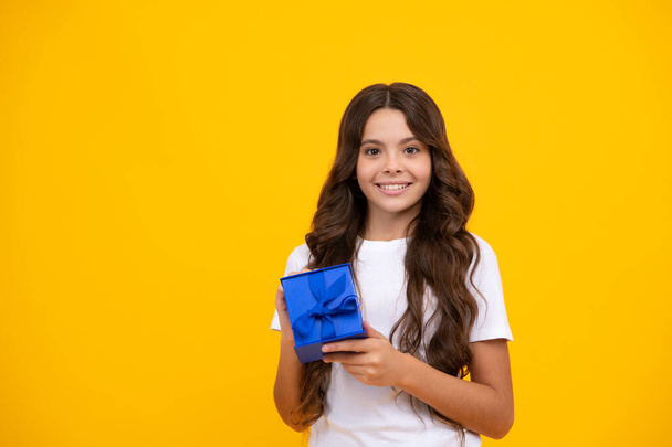 Porträt eines jugendlichen Mädchens, das eine Geschenkschachtel isoliert vor gelbem Studiohintergrund hält. Geschenk, Gruß und Geschenkidee. Geburtstagsferien-Konzept - Foto, Bild
