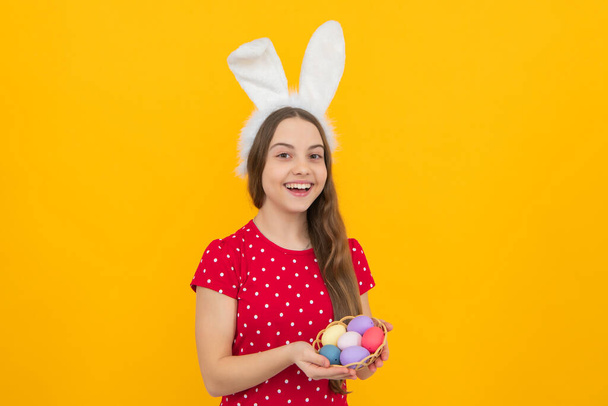 Концепція великодніх дитячих свят. Щаслива усміхнена маленька дівчинка-підліток з вухами кролика, що тримає розфарбовані великодні яйця
 - Фото, зображення