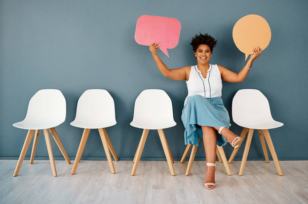 Tell me all about it. Studio portrait of an attractive young businesswoman holding up speech bubbles while sitting in line against a grey background - Photo, Image