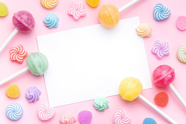Coloridas piruletas dulces y caramelos y tarjeta de felicitación vacía sobre fondo rosa. Piso tendido, vista superior - Foto, Imagen