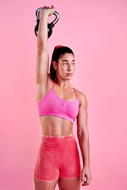 Lift it like you mean it. Studio shot of a sporty young woman exercising with a kettlebell against a pink background - Fotó, kép