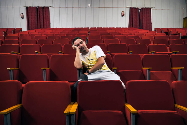 young man with glasses sleeping alone in cinema hall while everyone is gone. A lonely man in an empty theater fell asleep at the performance. An uninteresting boring opera. - Фото, изображение