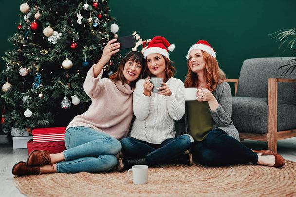 Bu fotoğraf çok güzel çıkacak. Noel zamanı evde cep telefonuyla kendi portresini çeken üç çekici orta yaşlı kadın. - Fotoğraf, Görsel