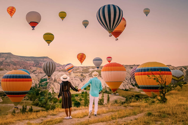 Gündoğumunda Kapadokya Türkiye, Goreme Capadocia Türkiye tepelerinde tatil yapan iki orta yaşlı erkek ve kadın, Kapadokya Türkiye 'de sıcak hava balonlarıyla güneşlenen erkekler ve kadınlar - Fotoğraf, Görsel