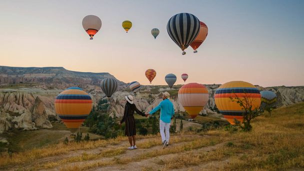 Kapadokya Kapadokya Türkiye, güneş doğarken Kapadokya Kapadokya 'nın sıcak hava balonlarını izleyen mutlu genç bir çift. - Fotoğraf, Görsel