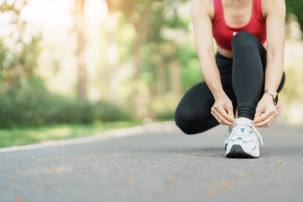Young athlete woman tying running shoes in the park outdoor, female runner ready for jogging on the road outside, asian Fitness walking and exercise on footpath in morning. wellness and sport concepts - Foto, immagini