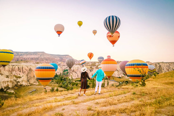 Cappadocia Turkey during sunrise, couple mid age men and woman on vacation in the hills of Goreme Capadocia Turkey, men and woman looking sunrsise with hot air balloons in Cappadocia Turkey - Photo, image
