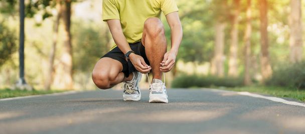 Young athlete man tying running shoes in the park outdoor, male runner ready for jogging on the road outside, asian Fitness walking and exercise on footpath in morning. wellness and sport concepts - Photo, Image