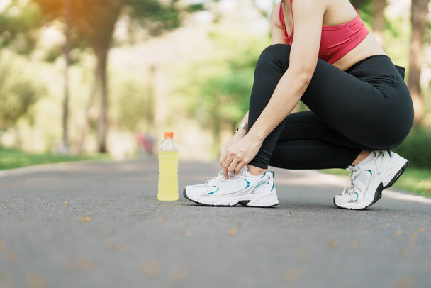 Fiatal sportoló nő futócipőt kötött Energy Drink vízzel, női futó kocogásra készen odakint, ázsiai Fitness séta és testmozgás a parkban reggel. wellness, jólét és sport koncepciók - Fotó, kép
