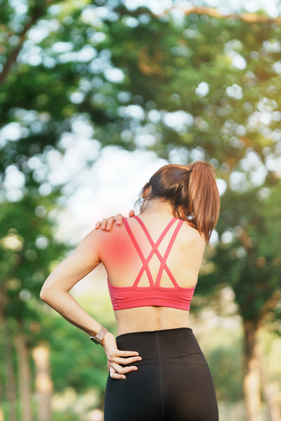 Young fitness woman holding her sports injury shoulder and neck, muscle painful during training. Asian runner female having body problem after exercise outside in summer - Photo, Image