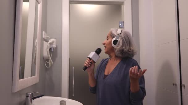 mujer feliz madura con el pelo gris, cantando en la bañera con micrófono que se divierte solo, después de la ducha - Metraje, vídeo