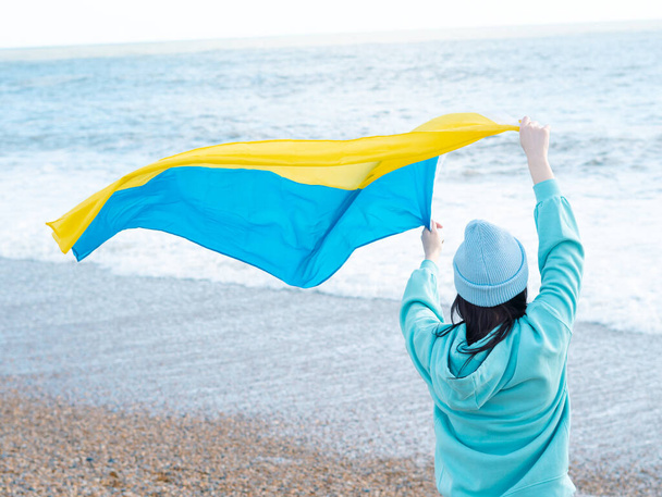 brunnete žena v modré mikině a modrém klobouku s národní vlajkou Ukrajiny, vlastenecký koncept - Fotografie, Obrázek