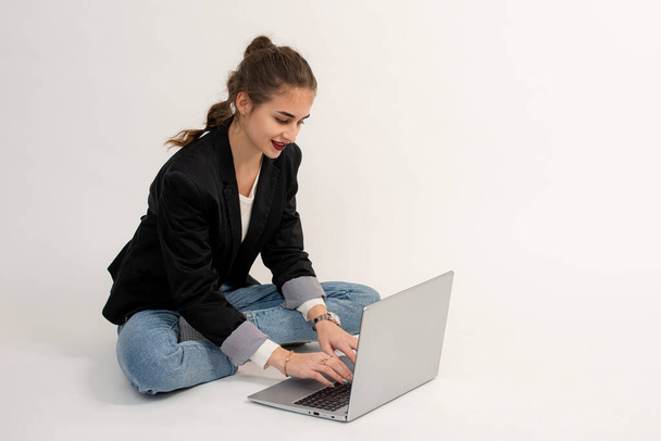 das Mädchen sitzt auf dem Boden und arbeitet oder kommuniziert auf einem Laptop. - Foto, Bild
