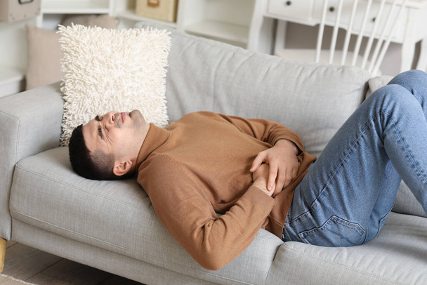 Jeune homme avec appendicite couché sur le canapé à la maison - Photo, image